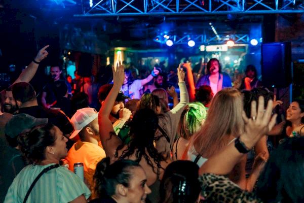 A crowd of people is dancing and enjoying live music at a vibrant, colorful nightclub or concert venue, with a band performing on stage.